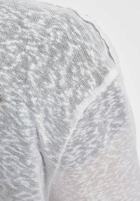 Weißer leichter Strickstoff mit strukturiertem Muster. Lockerer Webstil, der etwas Haut darunter sichtbar macht. Die Kanten wirken ausgefranst und sorgen für zusätzliche Details.