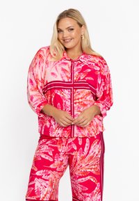 Kleurrijk, lang mouw, button-up shirt met een roze en rode bladzijden patroon en bijpassende broek met strepen aan de zijkanten. Gladde stof.