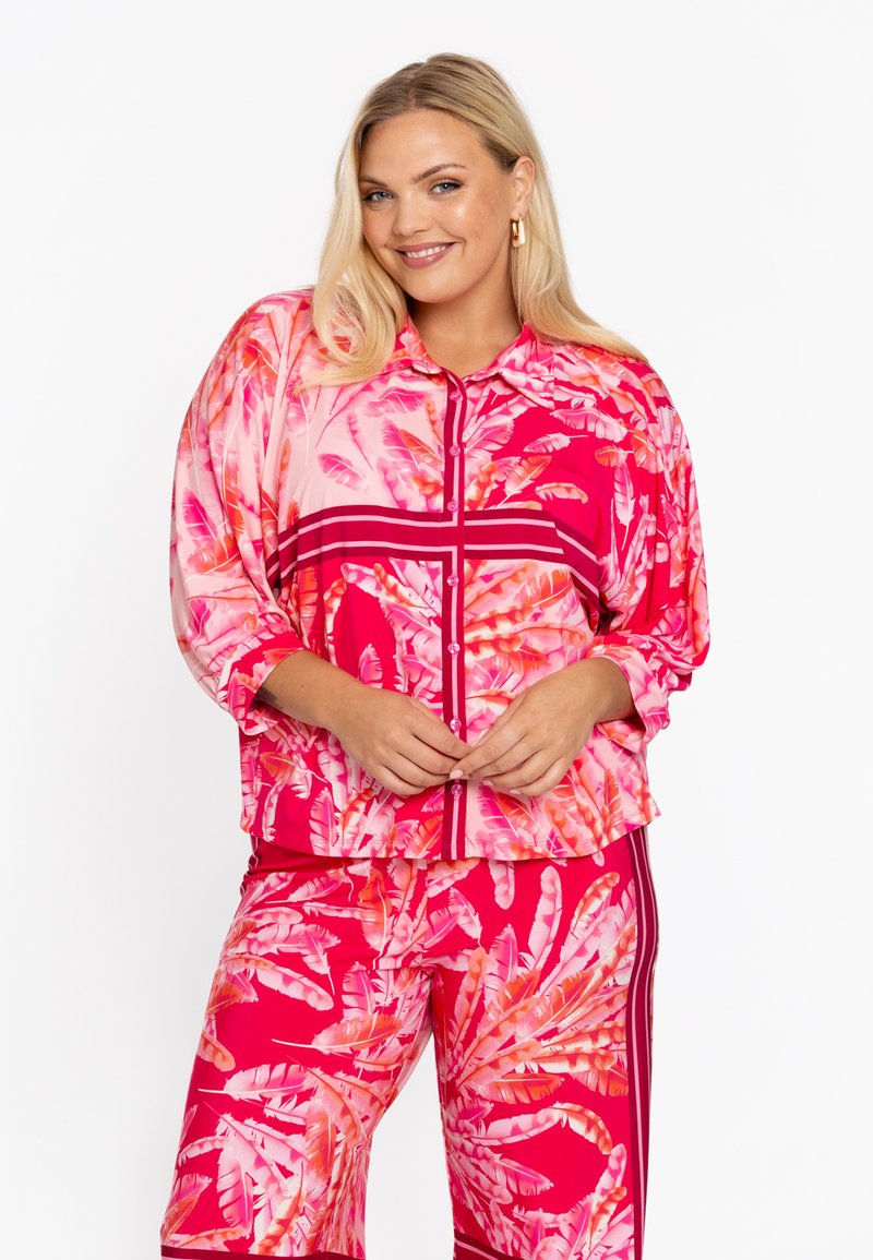 Kleurrijk, lang mouw, button-up shirt met een roze en rode bladzijden patroon en bijpassende broek met strepen aan de zijkanten. Gladde stof.