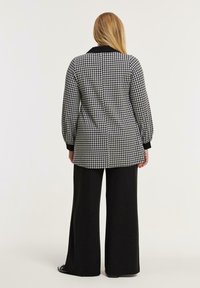 Schwarz-weiße Hahnentrittmuster Jacke mit schwarzem Kragen, langen Puffärmeln und schwarzen Akzenten, kombiniert mit schwarzen, weiten Hose.