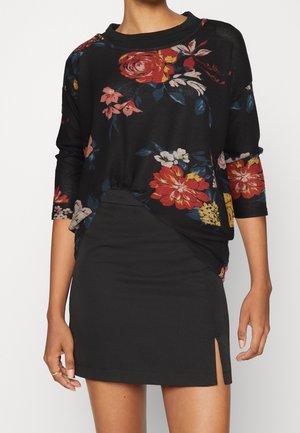 Schwarzes Blumenshirt mit drei Viertelärmeln, das mit roten, gelben und blauen Blumenmustern verziert ist; kombiniert mit einem eng anliegenden schwarzen Minirock mit einem seitlichen Schlitz.