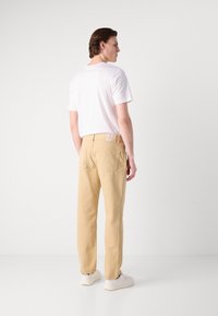 Pantaloni bej cu croială dreaptă, buzunare la spate și etichetă de marcă. Asortați cu un tricou alb simplu și adidași albi.