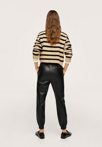 Gestreepte gebreide trui in beige en zwart, met een cropped ontwerp. Zwarte neplederen joggers met elastische manchet en zijzakken.