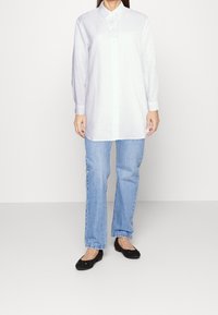 Langärmliges weißes Leinenhemd mit Knopfleiste, kombiniert mit hellblauen Jeans und schwarzen Ballerinas. Einfacher und lässiger Schnitt.