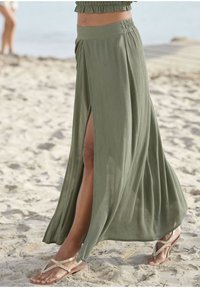 Olijfgroene maxi-rok gemaakt van lichtgewicht, gemêleerd weefsel met een hoge split en een elastische tailleband, gecombineerd met versierde slippers.
