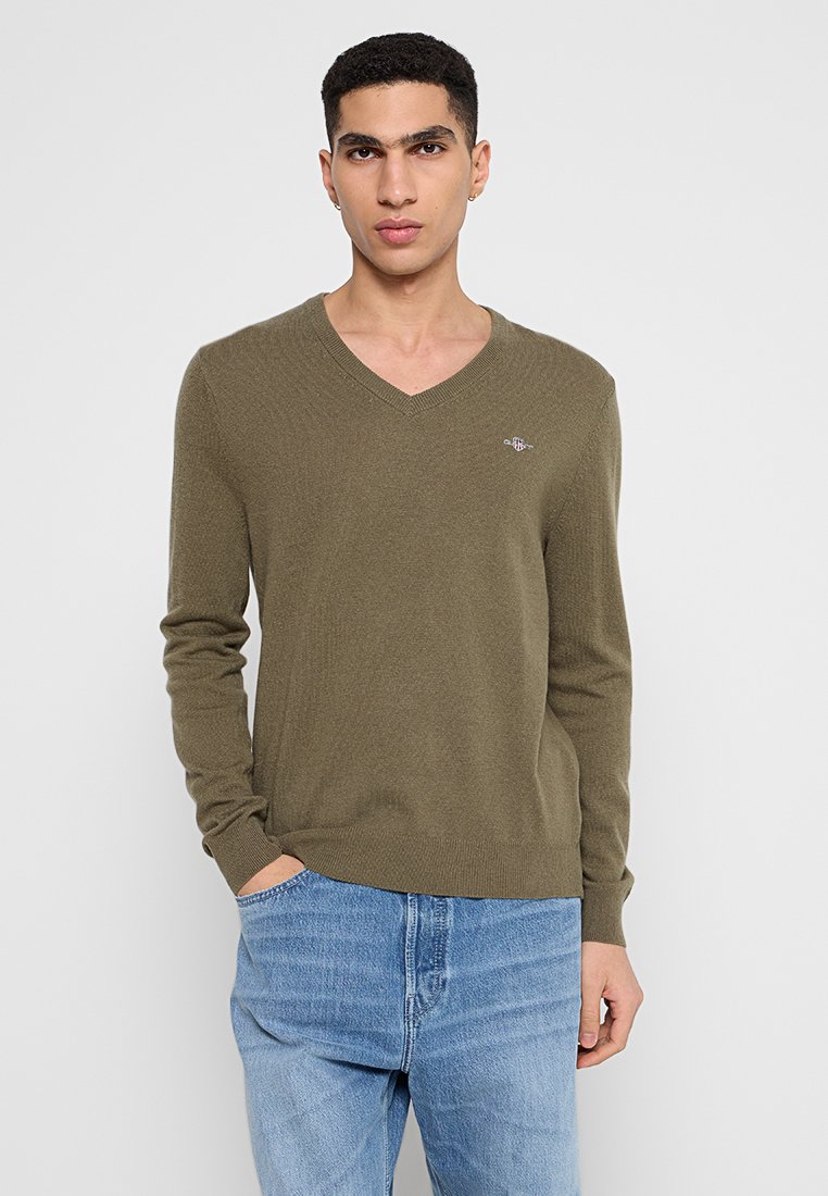 V-ringad tröja i olivgrön, tillverkad av mjukt stickat material. Har en ribbad yta, åtsittande ärmar och en liten logotyp på bröstet.