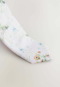 Slips med blomstermønster, der har en hvid baggrund med farverige blomster i nuancer af blå, orange og grøn, lavet af struktureret stof.