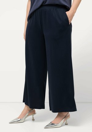 Marineblauwe wijde broek van zachte stof met een elastische tailleband. Bevat zijzakken en is gestyled met zilveren puntige hakken.