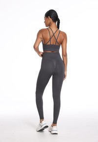 Sportowy szary biustonosz z krzyżującymi się ramiączkami, zestawiony z szarymi legginsami o wysokim stanie. Gładka tekstura, dopasowany krój i subtelne detale szwów.
