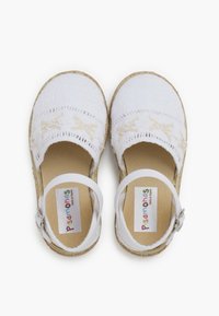 Baltos espadrilės su austine tekstile, ruda padas, reguliuojama balta juosta ir dekoratyvinė siuvinėjimo detalė priekyje.