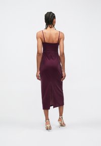 Robe midi mauve à fines bretelles, silhouette ajustée et fente dans le dos. Texture lisse, design épuré et style minimaliste.