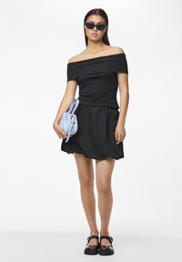 Črn off-shoulder rebrast top v kombinaciji s kratko črno krilo. Pohodni torbica svetlo modre barve in črne sandale z naramnicami dopolnjujejo outfit.