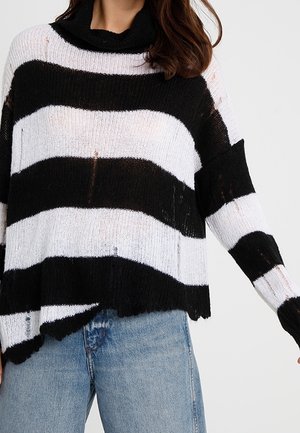 Pull en maille noir et blanc à rayures, coupe loose avec col camionneur, ourlet irrégulier et détails effilochés. Associé à un jean bleu.