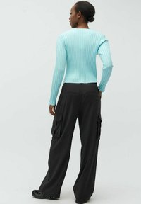 Hellblau gestreiftes Langarmoberteil, kombiniert mit locker sitzenden schwarzen Cargo-Hosen mit Seitentaschen, von hinten gezeigt.