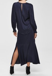 Mörkblå satinklänning med långa ärmar, nyckelhålsdetalj på ryggen och sidoklyfta, med en flödande maxi-längd och mjuk textur.