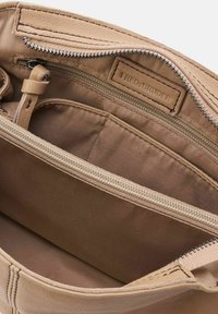 Intérieur d'un sac en cuir tan avec une poche zippée, texture lisse et une étiquette cousue à l'intérieur. Présente un revêtement en tissu brun et des tons neutres.