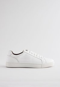 Baskets en cuir blanc à texture lisse, bout arrondi, semelle en caoutchouc plate et design à six œillets pour les lacets. Style minimaliste sans marque visible.