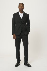 Completo tre pezzi nero con rever a punta, camicia bianca, pantaloni slim fit e scarpe di pelle nere. Texture liscia e design su misura.