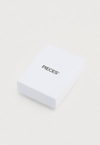 Λευκό ορθογώνιο κουτί με μαύρο λογότυπο «PIECES» στην κορυφή. Ομαλή υφή χωρίς επιπλέον σχέδια ή διακοσμήσεις.