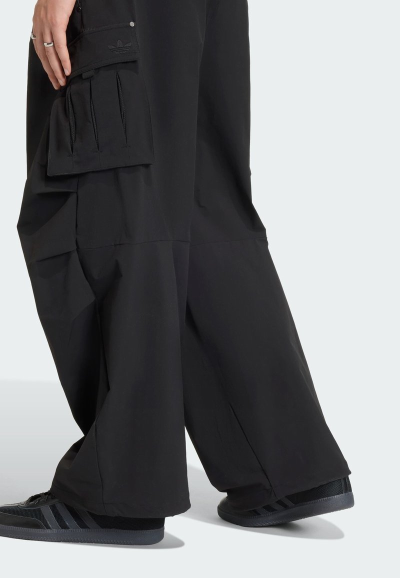 Svarta cargobyxor med vida ben, utrustade med en sidoficka, texturerat tyg och diskret märkning på fickan. Bärs med svarta sneakers.