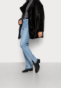 Abrigo de piel sintética negra, suéter de cuello alto gris, vaqueros de denim azul claro con dobladillos abiertos y botas negras de tobillo. Dise�ño simple y moderno.