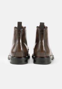 Stivali ankle in pelle marrone con finitura lucida, pannelli laterali elasticizzati e suole in gomma nere, dotati di una linguetta sul retro.