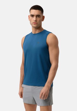 Blauw mouwloos sportshirt met een ronde hals, een gestructureerd oppervlak en een klein logo op de borst. Draagt met lichtgrijze shorts.