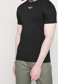 T-shirt noir à manches courtes en coton avec un col rond. Présente le logo "Calvin Klein Jeans" en blanc sur la poitrine.