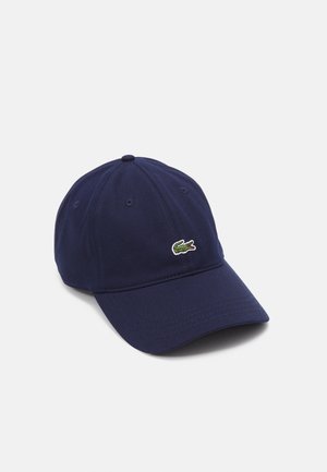 Navy blue baseball cap with small green crocodile logo on front, curved brim, and stitched eyelets for ventilation.