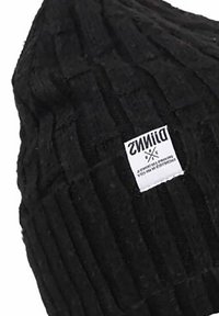 Berretto lavorato a maglia nero con una texture a coste. Presenta un'etichetta del marchio visibile e una parte superiore arrotondata. Il tessuto sembra spesso e caldo.
