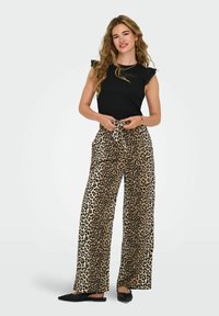 Haut noir sans manches avec détails à volants, associé à un pantalon large imprimé léopard beige et marron, complété par des chaussures noires à enfiler.