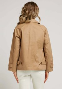 Veste beige en tissu lisse, avec un col classique, des boutons aux poignets, et une coupe décontractée avec un dos droit.