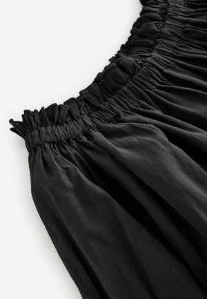 Črna krila z elastiko v pasu, ki se ponaša z nabranim materialom, gladko teksturo in tekočim dizajnom. Pas je naguban za dodatno podrobnost.