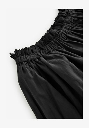 Črna krila z elastiko v pasu, ki se ponaša z nabranim materialom, gladko teksturo in tekočim dizajnom. Pas je naguban za dodatno podrobnost.