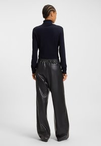 Navy turtleneck sweater with long sleeves paired with high-waisted black pleated faux leather pants, featuring an elastic waistband and back pocket.