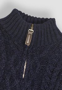 Maglione lavorato a maglia blu navy con colletto alto, caratterizzato da motivi a trecce e una cerniera corta con un tirante in pelle.