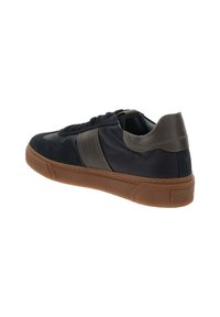 Zwarte leren en suède sneaker met een bruine rubberen zool, vetersluiting en contrasterende stofpaneel aan de zijkant. De achterkant heeft een lichte hak.