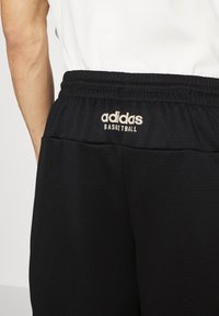 Schwarze Mesh-Basketballshorts mit elastischem Bund, ausgestattet mit einem geprägten "adidas BASKETBALL"-Logo in Hellbeige.