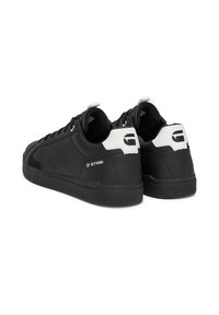 Melni sintētiskie sporta apavi ar gludu tekstūru, apaļu purngalu un baltām akcentiem uz papēža. Satur logotipa detaļu netālu no papēža un perforācijas.