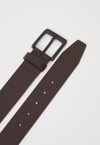 Ceinture en cuir brun avec une boucle rectangulaire en métal noir, arborant un logo de marque. La sangle comporte cinq trous et une extrémité effilée.