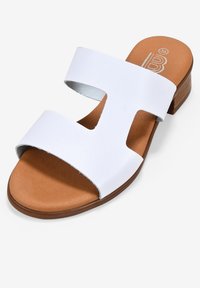 Sandalias blancas de punta abierta que presentan dos correas anchas, una plantilla acolchada de color marrón claro y un tacón bajo y cuadrado para mayor estabilidad.