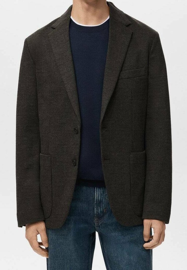 Homme portant un blazer à carreaux foncé sur un pull bleu marine et un jean bleu, debout avec les mains détendues le long du corps.