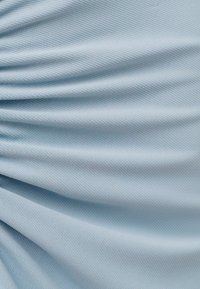 Hellblauer Stoff mit feiner gewebter Textur, der weiche Falten und sanfte Schatten über die Oberfläche bildet.