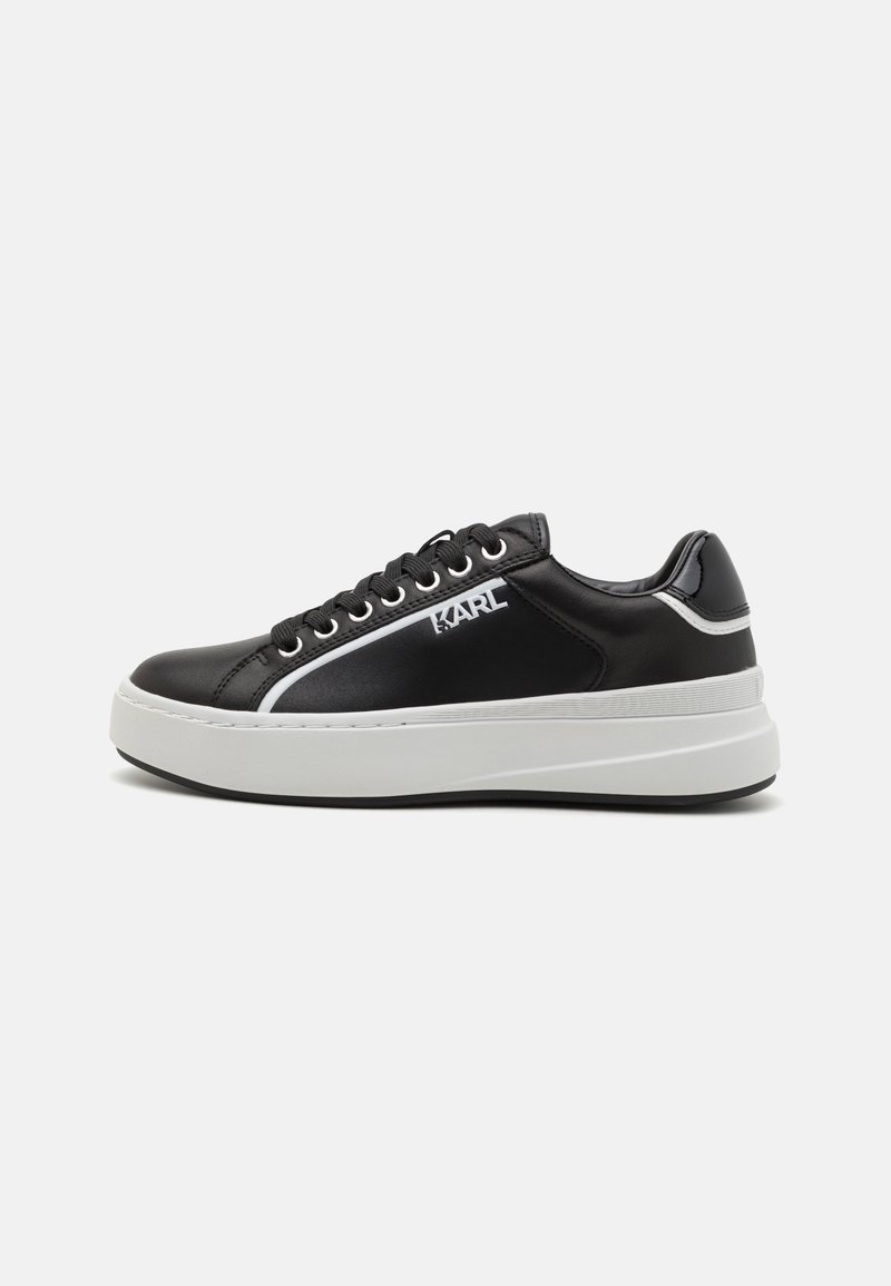 Musthave musta sneaker, millel on läikiv nahk ülemine osa, valge platvormi tald, tikandiga logo ja kontrastsed valged külgpaneelid. Paeltega disain.