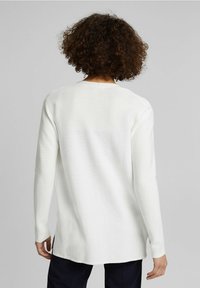 Bílý svetr s dlouhými rukávy a kulatým výstřihem, s texturovaným vzorem. Postranní rozparky na spodním lemu; měkká tkanina, uvolněný střih.