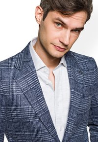 Granatowa marynarka w kratę z teksturowanej tkaniny z szpiczastymi klapami, zestawiona z jasnoszarym koszulą z guzikami, z kołnierzykiem i widocznymi guzikami.