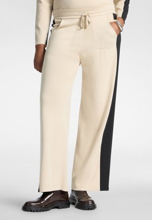 Pantaloni crema a gamba larga con pannelli laterali neri, indossati con stivali chunky marrone scuro e top crema con maniche.