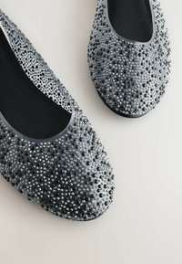 Harmaat ballerinat, joissa on sileä, pyöreä kärki. Pinta on peitetty kiiltävillä mustilla ja hopeisilla niitteillä, musta sisus ja joustava pohja.