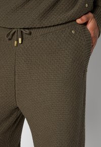 Braune strukturierte Jogginghosen mit einem elastischen Bund und Zugband, ausgestattet mit goldfarbigen Hardware-Akzenten. Nahaufnahme.