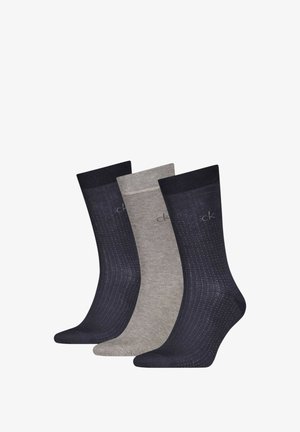 Tre paia di calzini alla caviglia: uno blu navy con motivo a pois, uno grigio chiaro e uno grigio scuro, tutti con bordi a coste e superficie liscia.